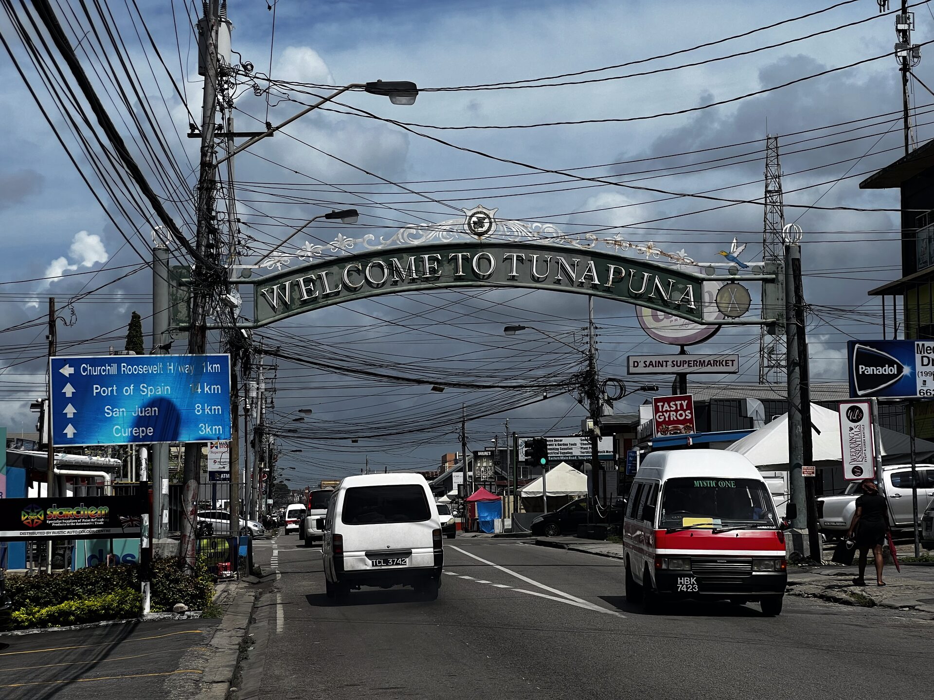The Welcome to Tunapuna arch over the Eastern Main Road, with maxi taxis and traffic beneath it.
